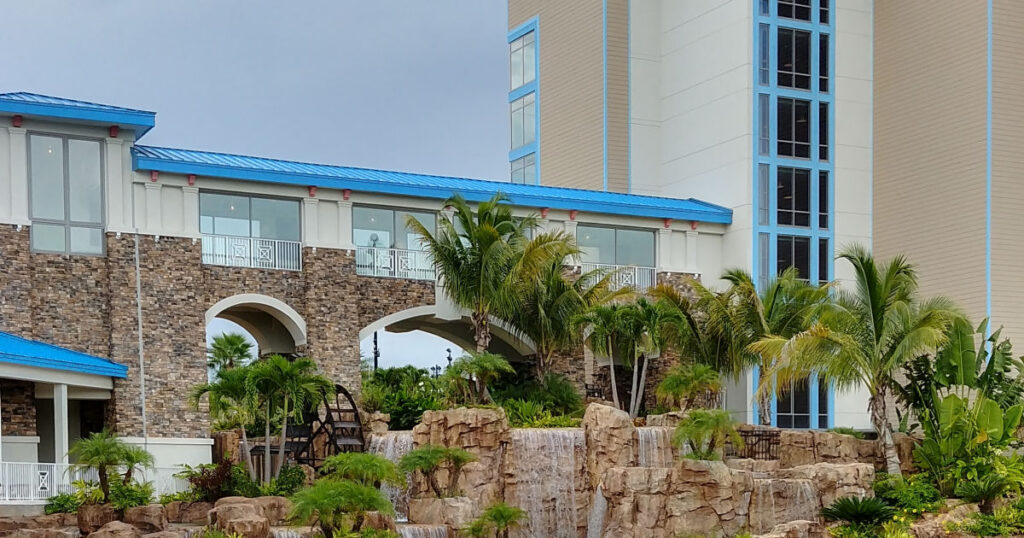 luscious green palm trees blowing in the breeze with a waterfall along a resort walkway
