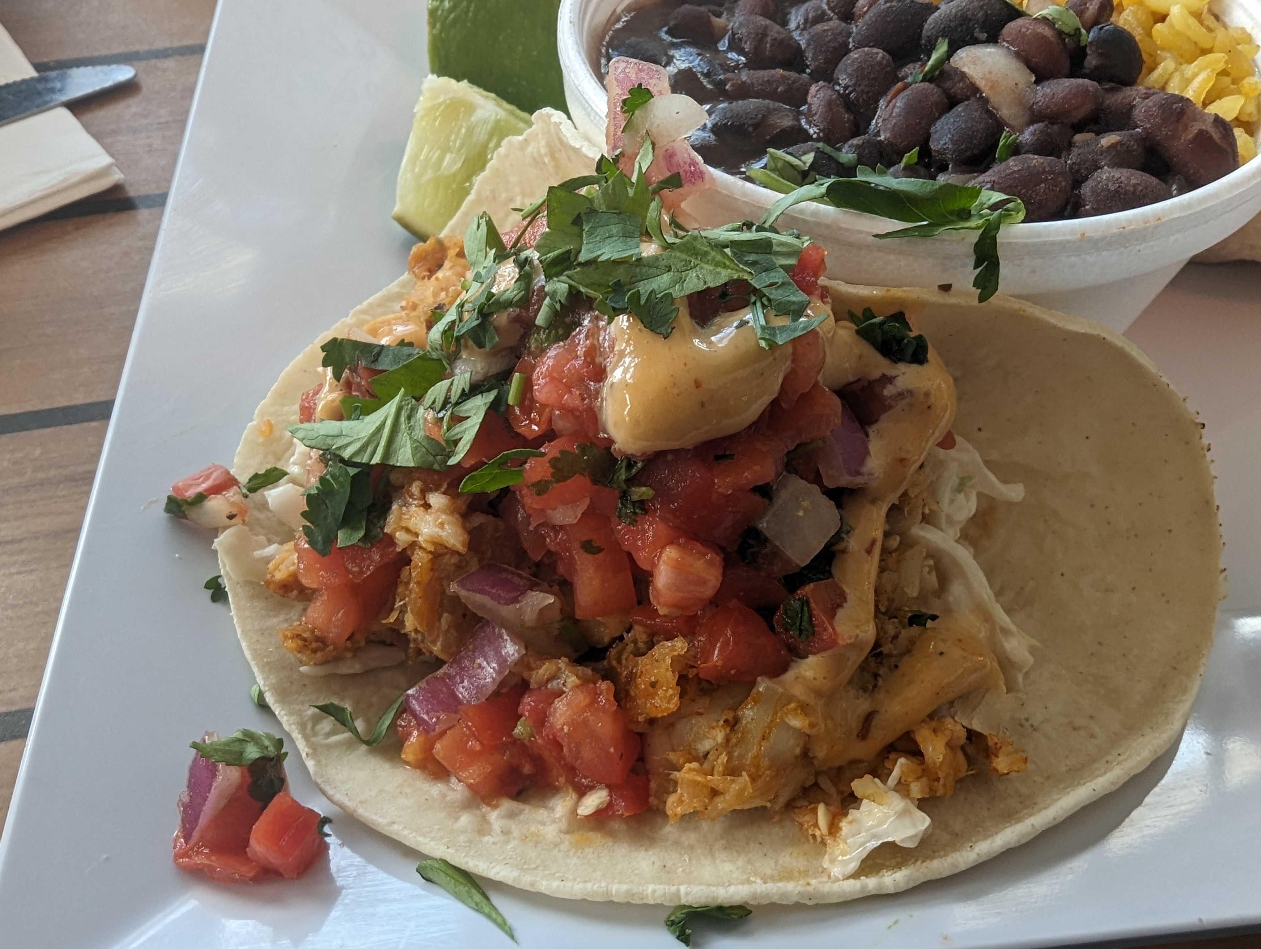 Round Tortilla with chicken, tomatoes, onion, cilantro on a white plate with a round bowl of black beans