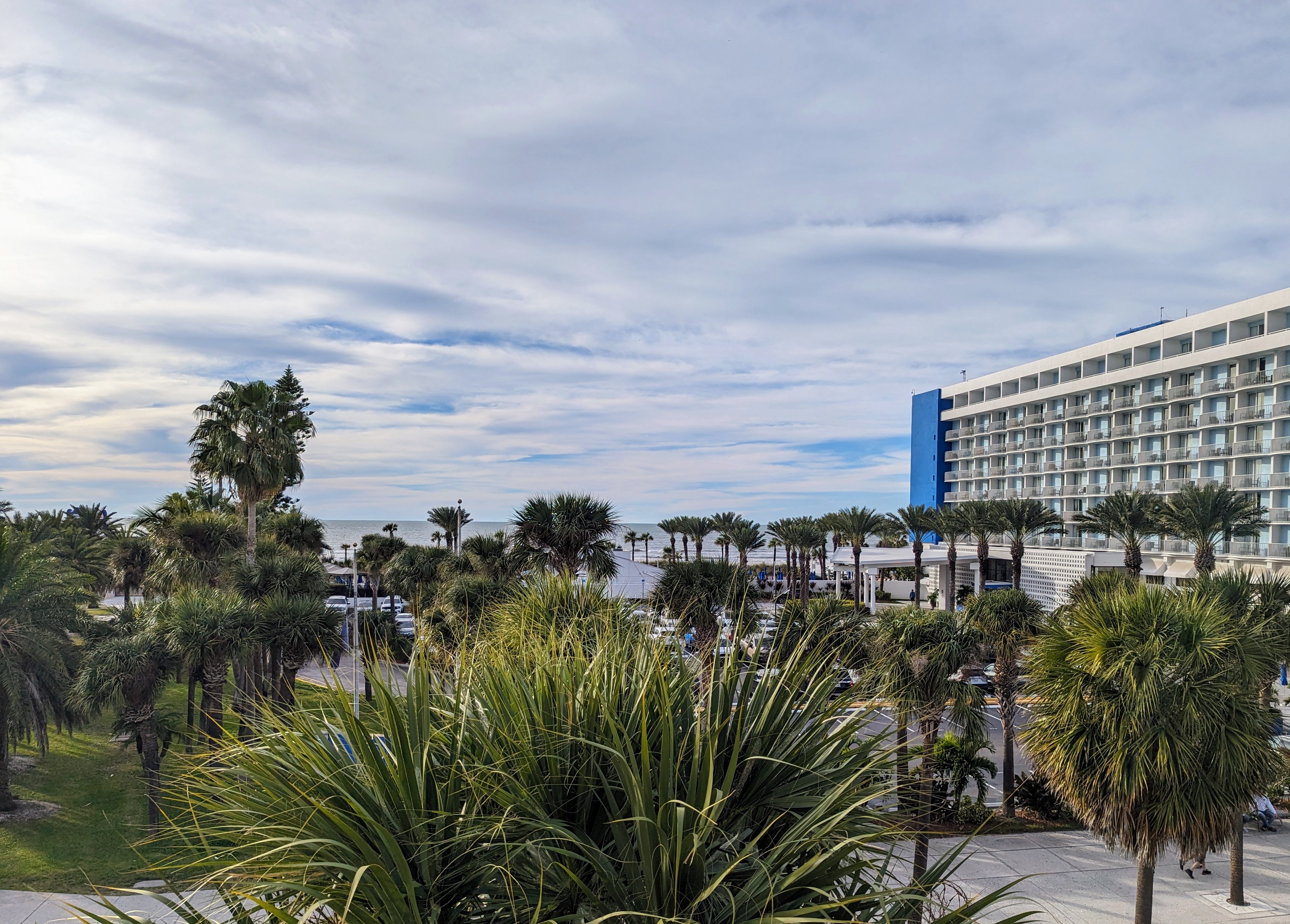 photo of a hotel by the beach with palm trees and clouds in the sky