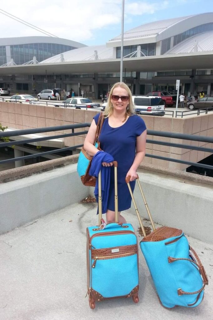 woman with a blue dress and sunglasses with turquoise luggage standing in front of an airport